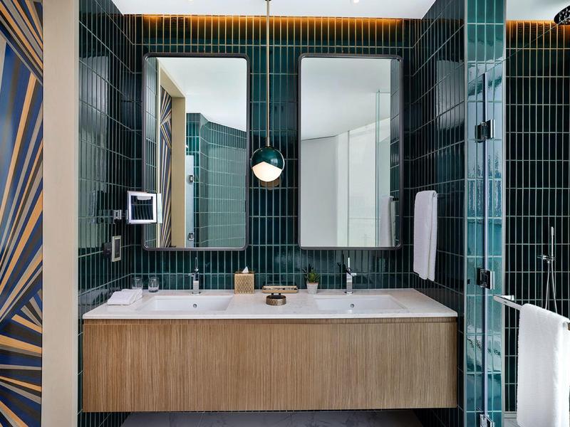 Modern hotel bathroom with double sink, green tiles, and wooden cabinet