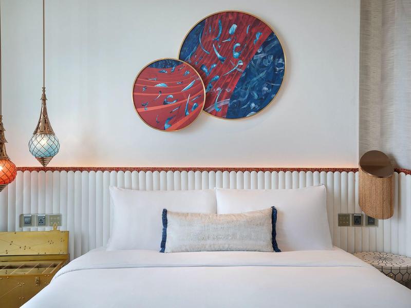 Modern hotel room with double bed, decorative round wall art, and two hanging lamps.