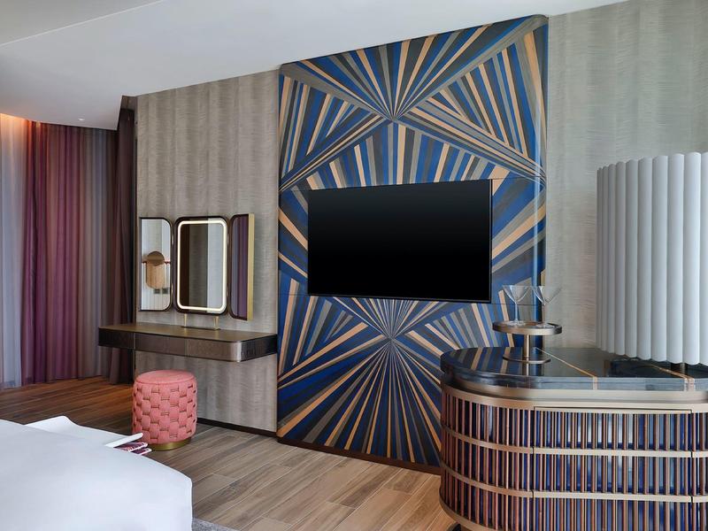 Modern hotel room with TV, designer dresser, and mirror on the vanity desk.
