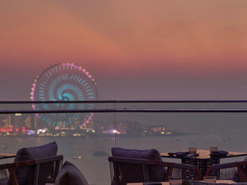 View of café terrace with empty tables and Ferris wheel at sunset by the water