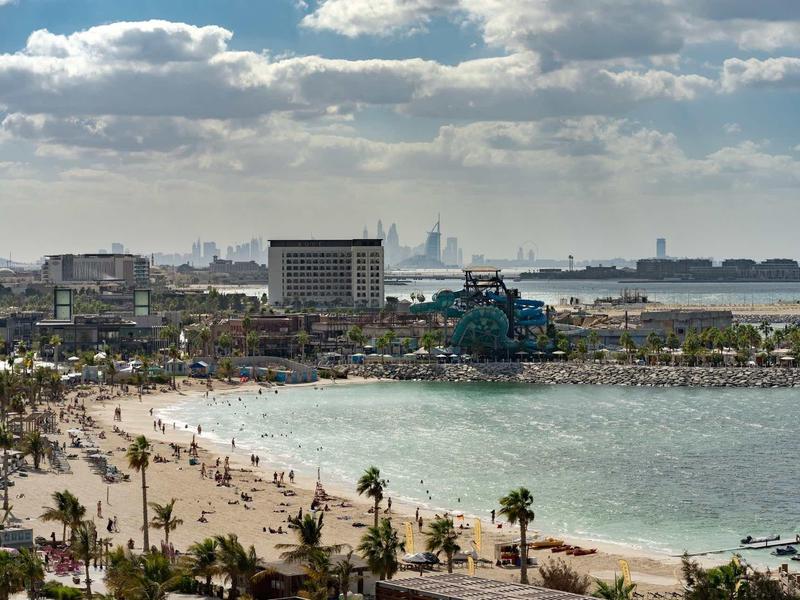 Pláž s mnoha lidmi, palmami a městským panoramatem pod zataženou oblohou