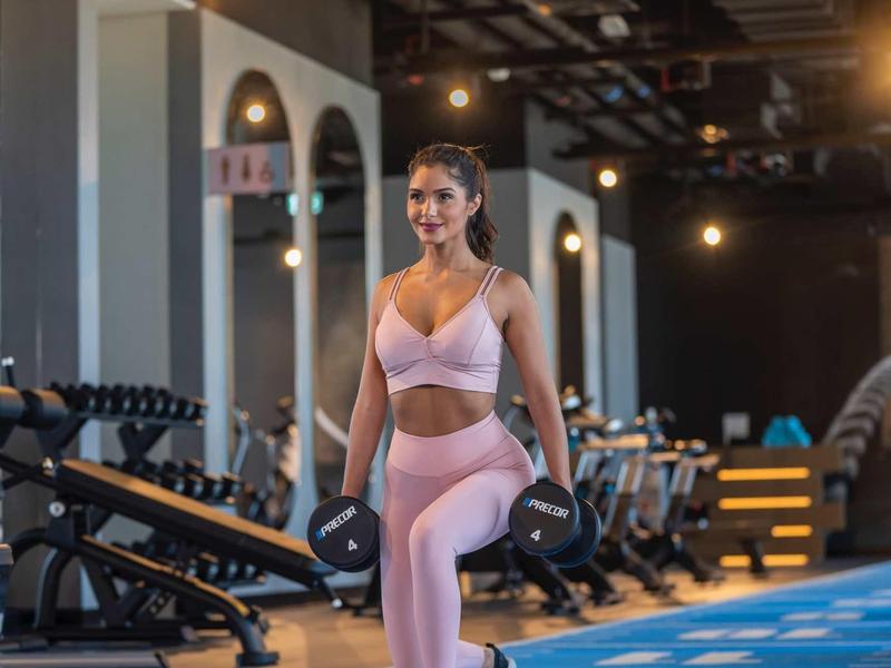 Žena v růžovém sportovním oblečení cvičí s činkou v posilovně.