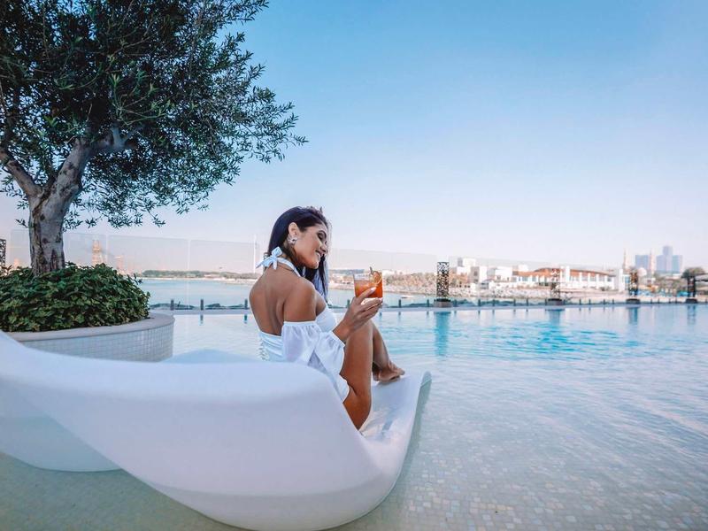 Žena relaxuje u bazénu s výhledem na město při západu slunce.