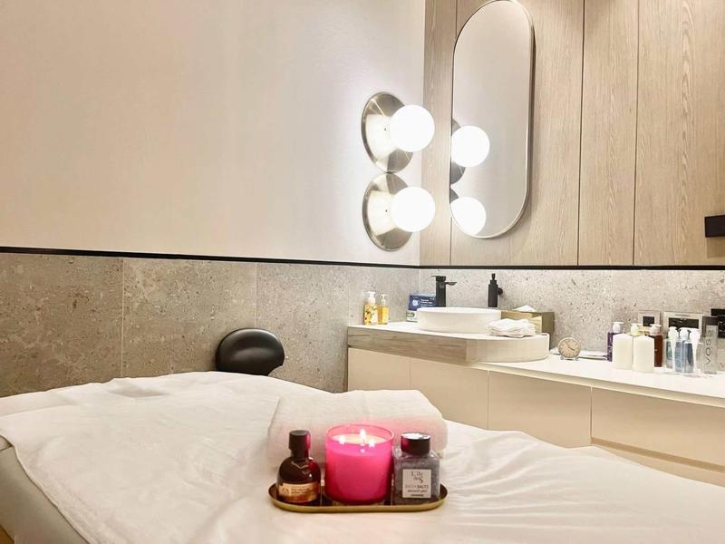 Pohodlná wellness místnost s masážním lůžkem, svíčkami a koupelnovými produkty v světlém prostředí.