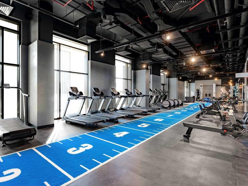 Moderní posilovna s běžeckými pásy a posilovacími stroji vedle modré dráhy.