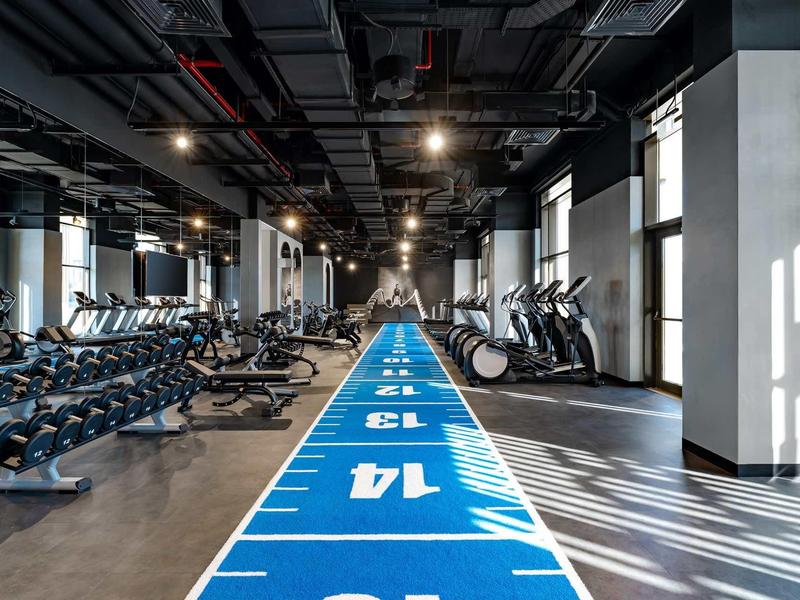 Moderní fitness s činkami, koly a modrou tréninkovou dráhou v hotelu.