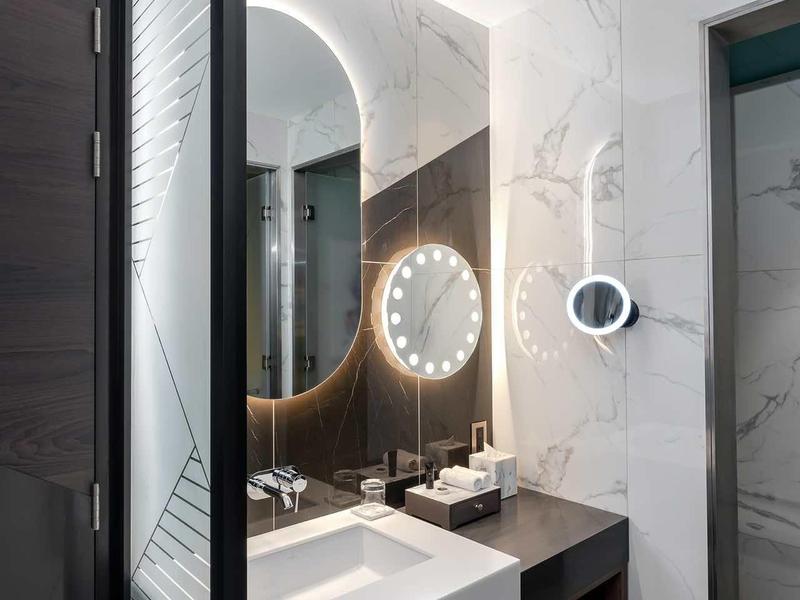 Moderní koupelna s osvětleným zrcadlem, umyvadlem a odpadkovým košem v stylovém designu.