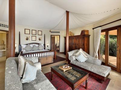 Elegant bedroom with four-poster bed, two lounges, and large windows overlooking greenery.