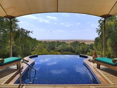 Infinity pool overlooking green vegetation under a blue sky, surrounded by wooden deck.