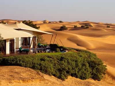 Luxury desert camp with tents and terraces amid a vast sand dune landscape.