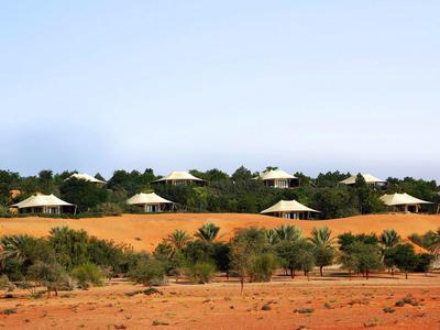 Desert resort with several white tents surrounded by greenery under clear skies.
