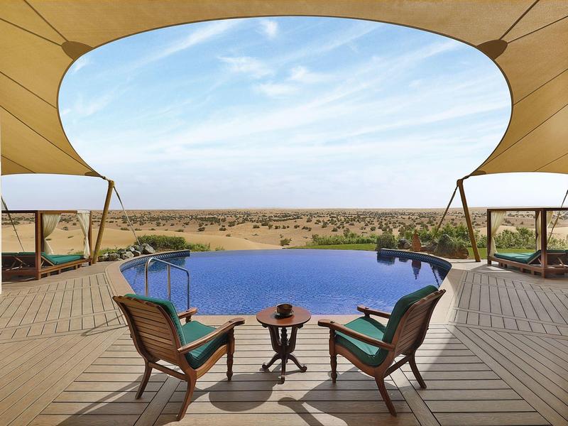 Lounge area with pool, comfortable chairs, and view of vast desert landscape.