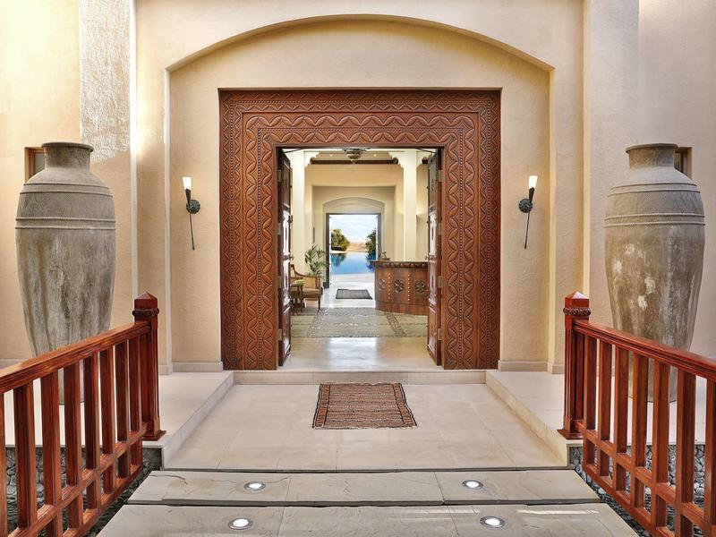 Elegant hotel corridor with wooden railings, large vases, and view through to a pool.