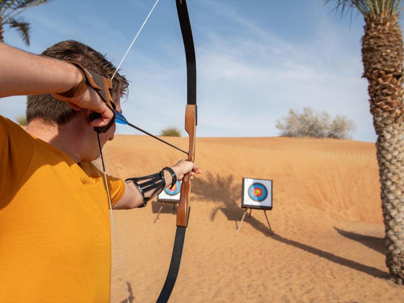 Young man shooting a bow and arrow at a target in a desert landscape.