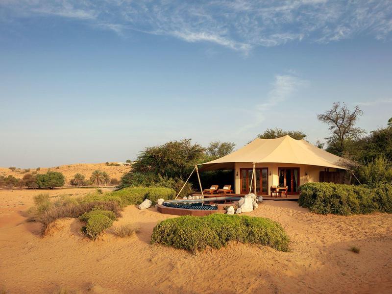 Luxury tent with deck and lounge chairs in a desert landscape.