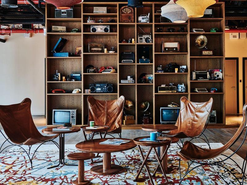 Modernes Wohnzimmer mit braunen Ledersesseln, runden Holztischen und großer Regalwand voller Dekoration.