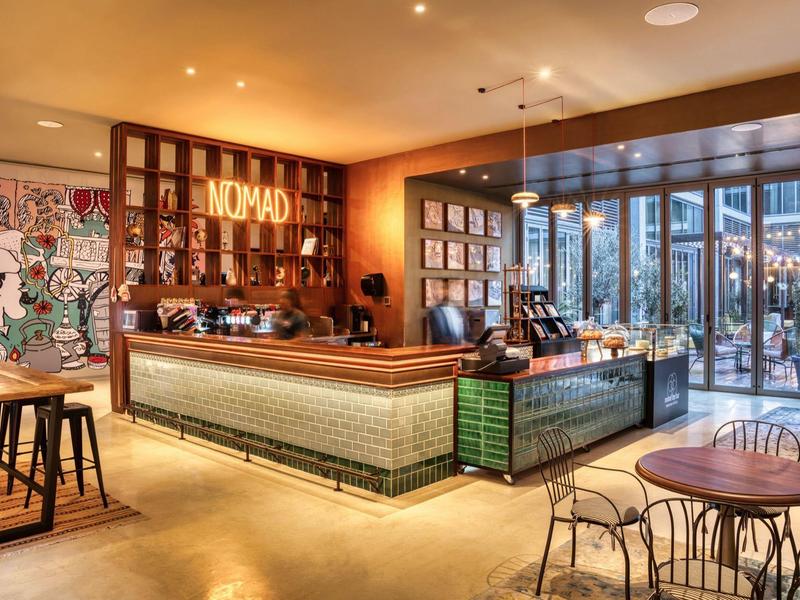 Moderne Bar mit Holztheke, Wandregalen, buntem Mosaik und großen Fenstern mit Stadtblick.