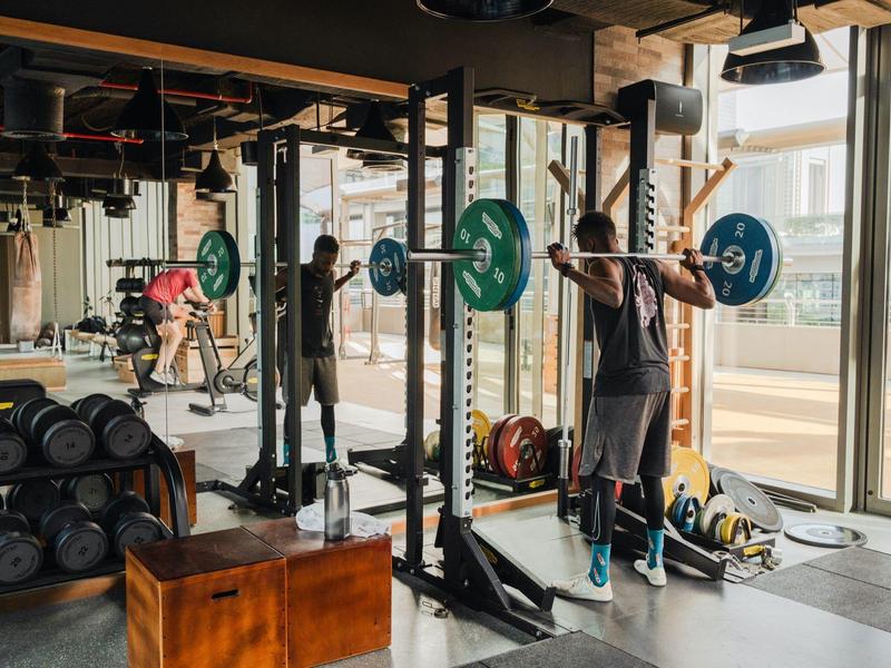 Fitnessstudio mit Hanteln, Spiegeln, großen Fenstern und zwei Personen beim Gewichtheben.