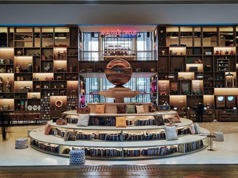 Große Bibliothek mit einer spiralförmigen Bücherinsel und einer großen Globen-Skulptur in der Mitte.