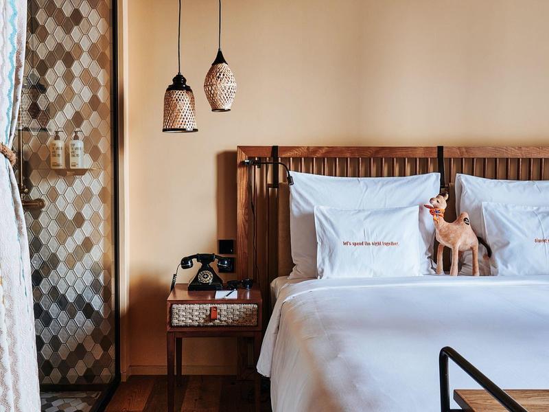 Gemütliches Schlafzimmer mit weißem Bett, Holzkopfteil, Nachttisch und zwei hängenden Lampen.