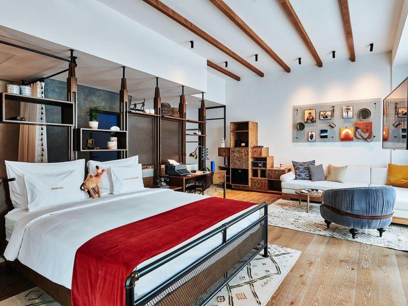 Helles, modernes Schlafzimmer mit Holzdecke, großem Bett, roter Tagesdecke und gemütlicher Sitzecke.