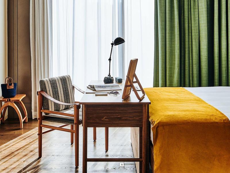 Gemütlicher Raum mit Holzmöbeln, grünem Vorhang und gelber Tagesdecke auf dem Bett.