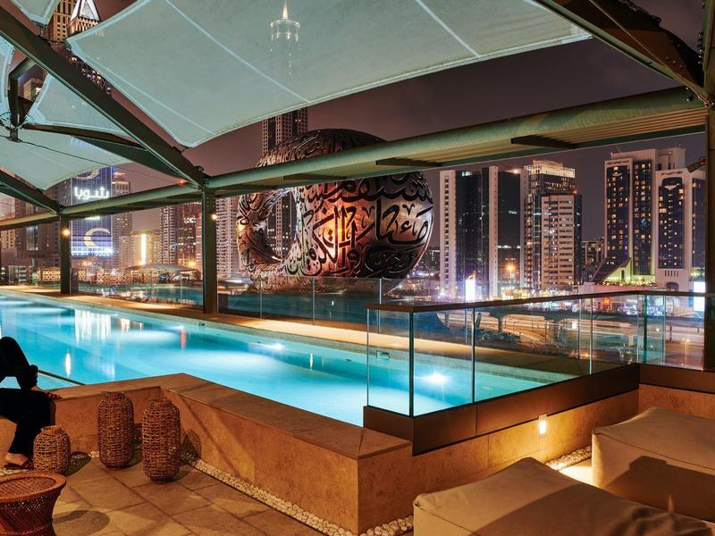 Moderner Pool auf Dachterrasse mit Stadtblick, Glasgeländer und gemütlichen Sitzplätzen bei Nacht.