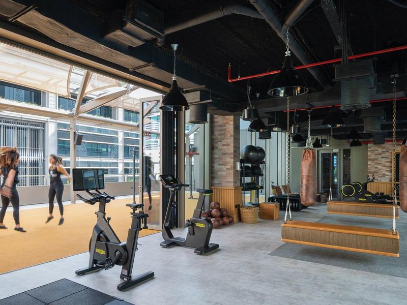 Moderne Fitnessstudio mit Boxsäcken, Fahrrädern und zwei Frauen beim Training auf gelbem Boden.