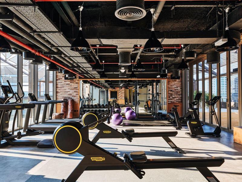 Moderner Fitnessraum mit Laufbändern, Rudergeräten, Hanteln und großem Fensterfront.