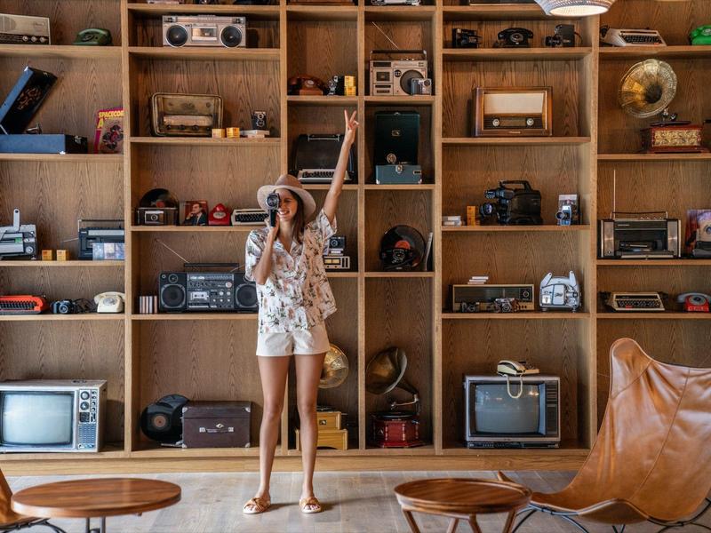 Frau steht vor großer Holzwand mit Regalen voller Vintage-Radios und Fernseher, angrenzend Lederstuhl.