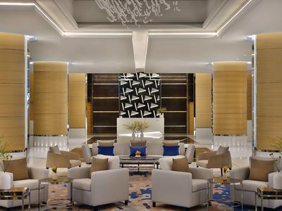 Elegancka przestrzeń hotelowego lobby z jasnymi fotelami, stołami i nowoczesnym oświetleniem.