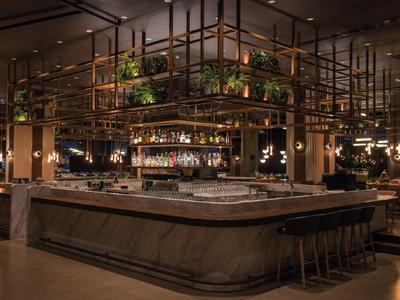 Nowoczesny bar koktajlowy z centralnym barem i wiszącymi roślinami w ciepło oświetlonym hotelu.