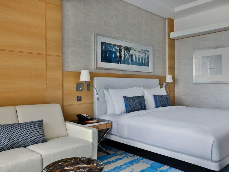 Modernes Hotelzimmer mit Doppelbett, weißem Sofa, Holzwand und Kunstwerken an grauen Wänden.