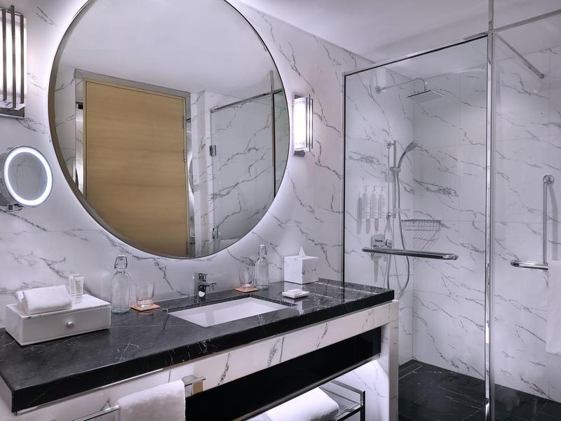 Modernes Badezimmer mit rundem Spiegel, schwarzer Arbeitsplatte und Glasdusche mit weißen Marmorwänden.