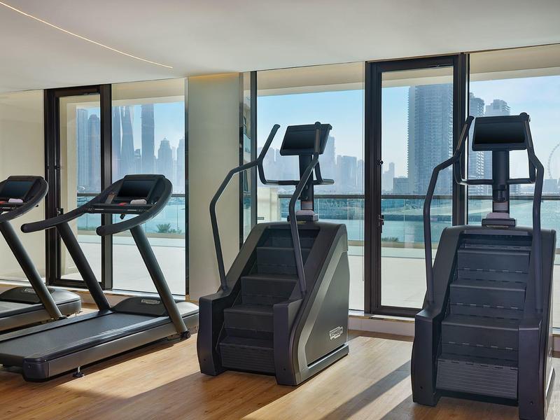 Moderner Fitnessraum mit Laufbändern und Steppern vor großen Fenstern mit Stadtblick.