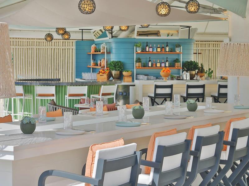 Moderner Essbereich mit langem weißem Tisch, bunten Stühlen und türkisfarbener Wand im Hintergrund.