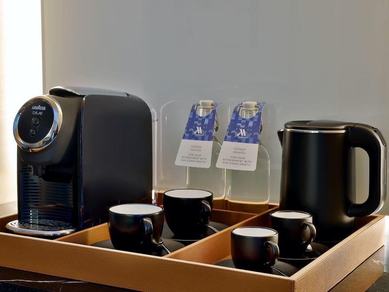 Tablett mit Kaffeemaschine, Tassen, Wasserflaschen und elektrischem Wasserkocher in einem Hotelzimmer.