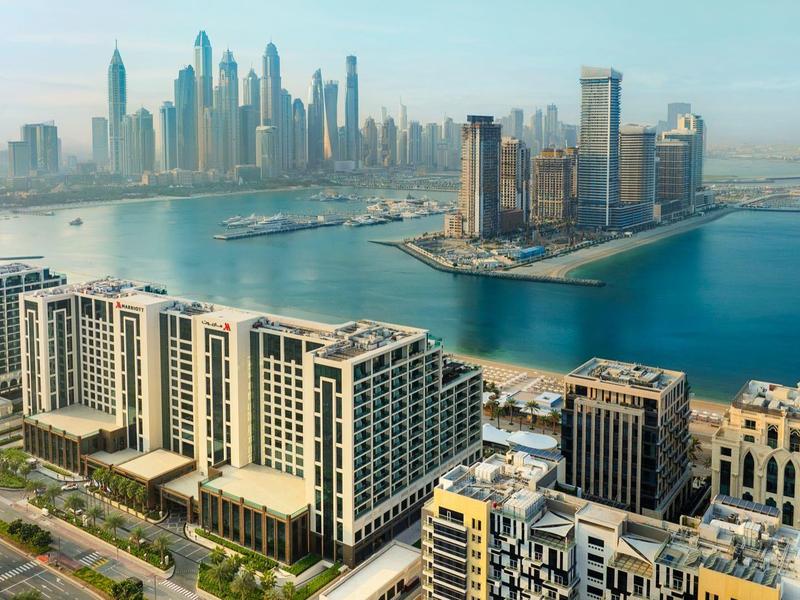 Stadtansicht mit modernen Hochhäusern, Wasserflächen und bewölktem Himmel im Hintergrund.