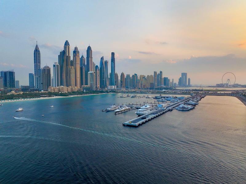 Blick auf moderne Wolkenkratzer und Yachthafen am Wasser bei Sonnenuntergang.