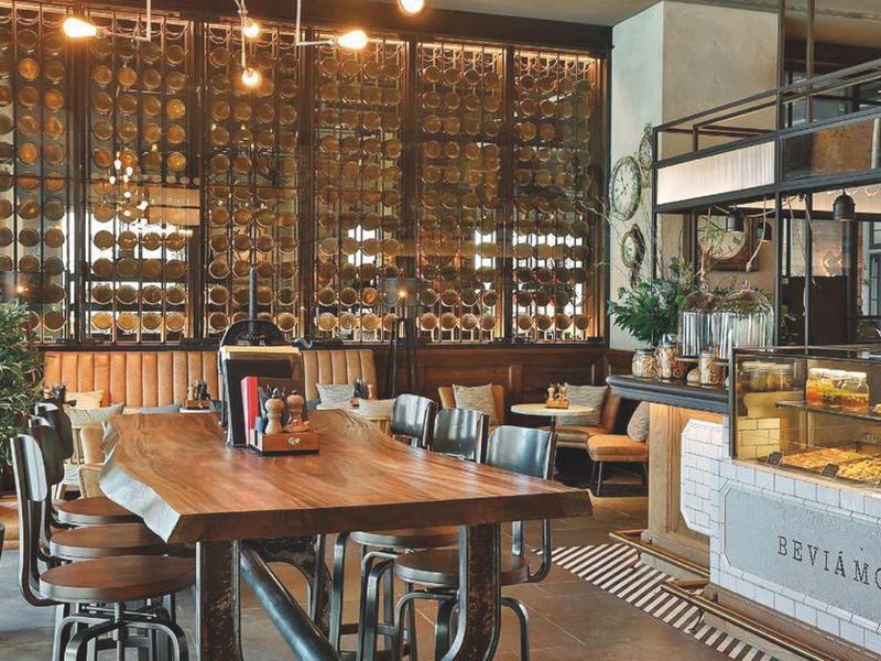 Moderner Hotel- oder Restaurantbereich mit Holztischen, Weinregalen und gemütlicher Beleuchtung.