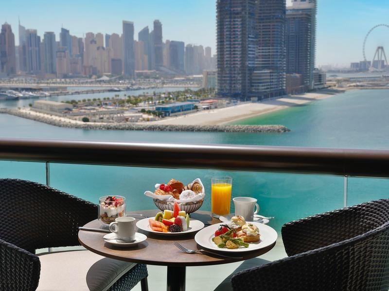 Balkontisch mit Frühstück vor Meer, moderner Skyline und Freizeitpark im Hintergrund.