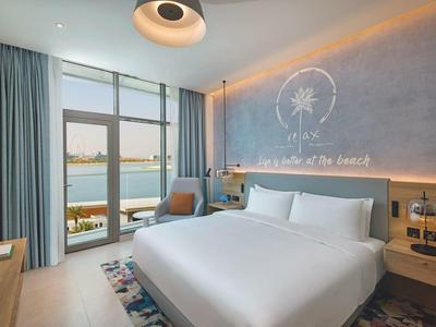 Modernes Schlafzimmer mit großem Bett, blauen Vorhängen und Glasfenster mit Seeblick.