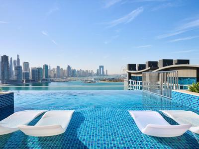 Infinity pool with lounge chairs overlooking the city by the water under clear sky.