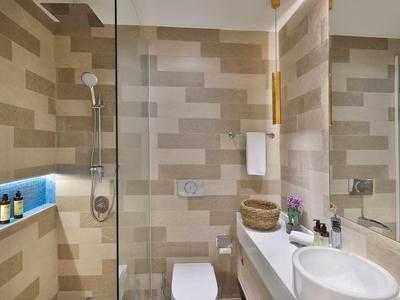 Modernes Badezimmer mit beigen Fliesen, Glasdusche, weißem WC und Waschbecken, Spiegel und Ablageflächen.