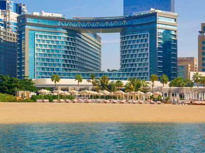 Modernes Hotel mit blauer Glasfassade an einem Sandstrand und klarem blauem Meer.
