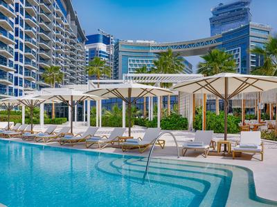 Nowoczesny hotelowy basen z leżakami i parasolami przed wysokimi szklanymi budynkami