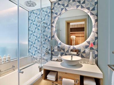 Modernes Badezimmer mit geometrischer blauer Wandfliese, rundem beleuchtetem Spiegel und weißem Waschbecken.