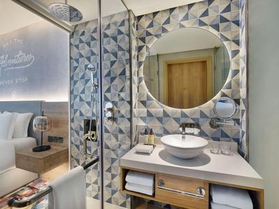 Nowoczesna łazienka z okrągłym lustrem, białą umywalką i geometrycznymi płytkami ściennymi.