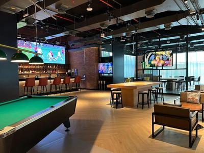 Nowoczesna strefa rekreacyjna z stołem bilardowym, barem, miejscami do siedzenia i dużymi ekranami.