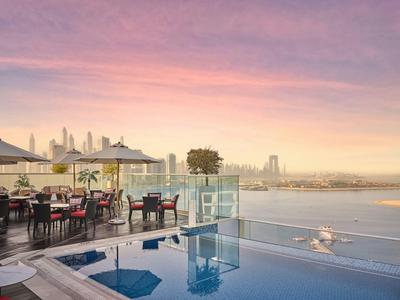 Rooftop terrace with pool, tables, and city view at sunset.